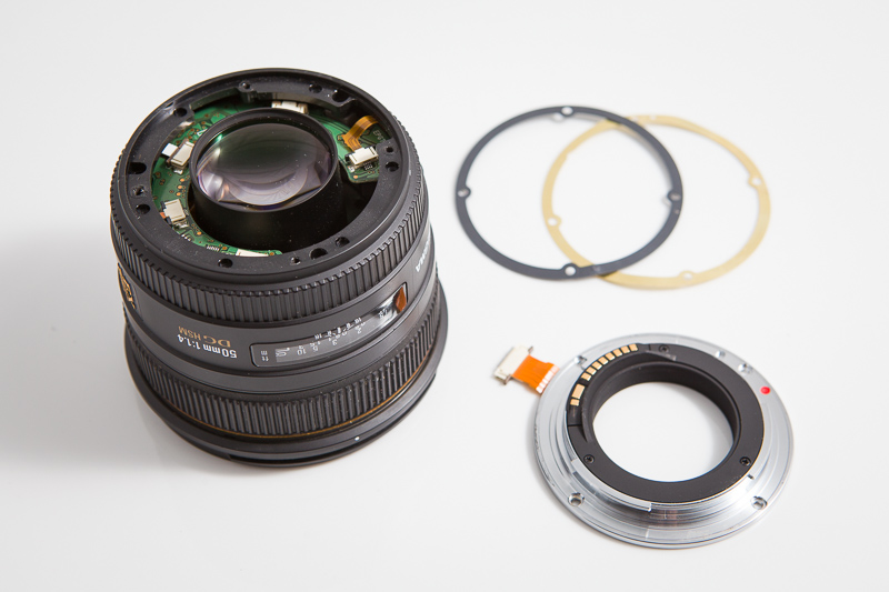 Sigma 50 mm F1,4 EX DG HSM s ulomenou objímkou. V pozadí můžete vidět kroužky, které se do objektivu vkládají pro přesné seřízení vzdálenosti čoček od senzoru - hraje se zde o zlomky milimetru.jpg