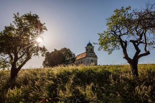 Jak vylepšit kompozici fotografie: širší záběr kapličky orámované stromy.