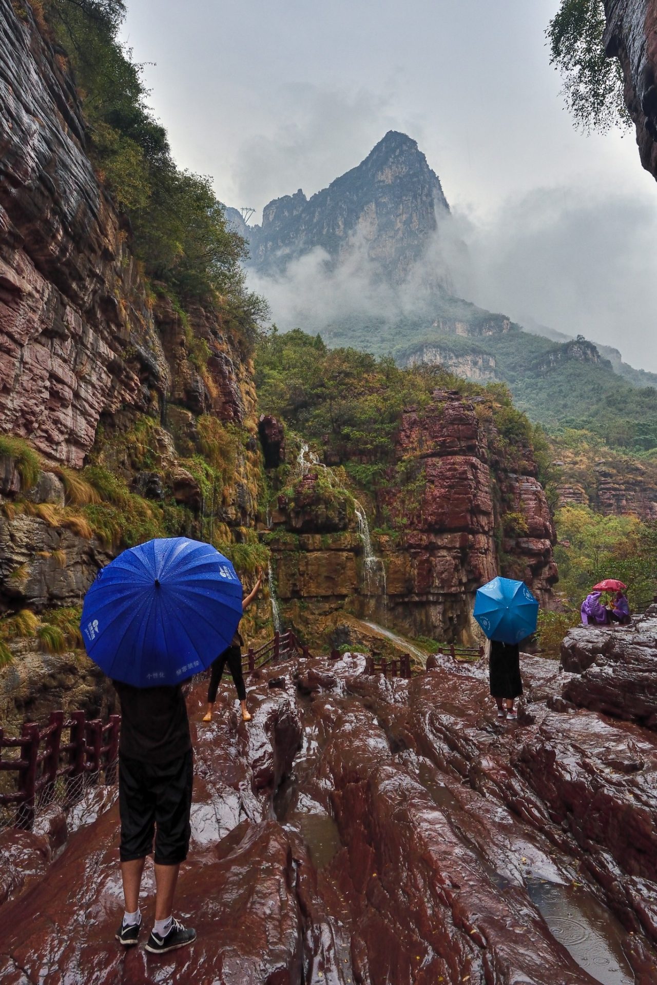 Čína, lidé s deštníky, kluzké skály